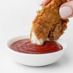 front-view-hand-dipping-fried-chicken-ketchup_23-2148682829